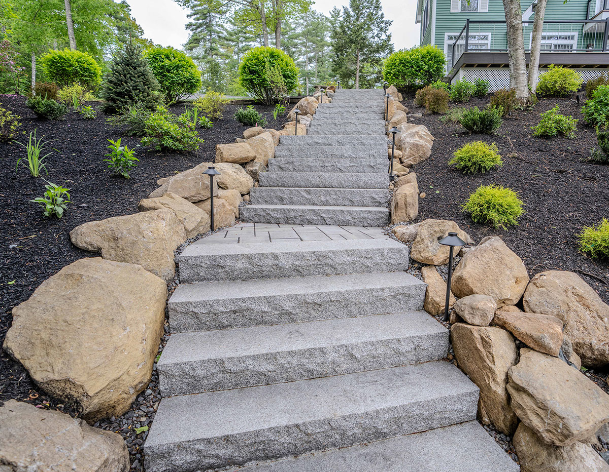 Dry-stacked natural stone retaining wall with integrated garden steps and ornamental grasses